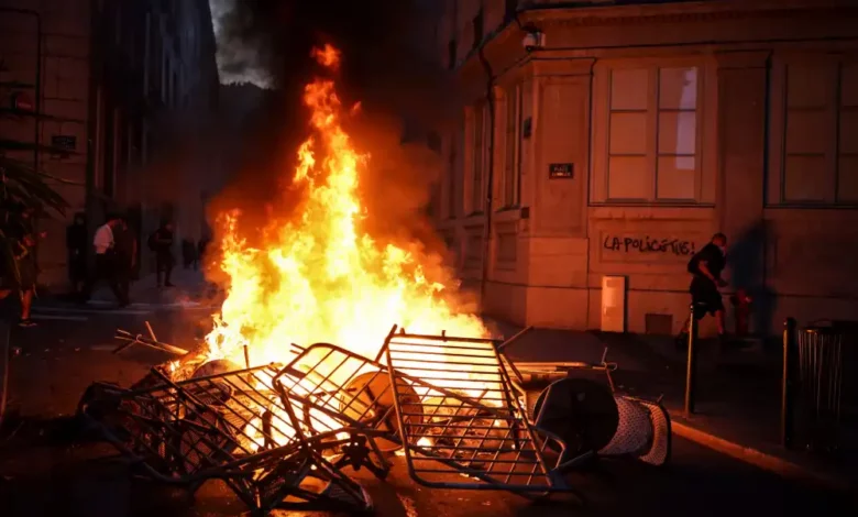 Un hombre pasa por delante de una pared iluminada por una barricada en llamas, con una pintada con la frase "La policía mata", en el centro de Lyon. 